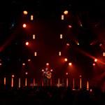 Trivium乐队主唱Matt Heafy站在灯光昏暗的舞台上，在一大群人面前弹着原声吉他.